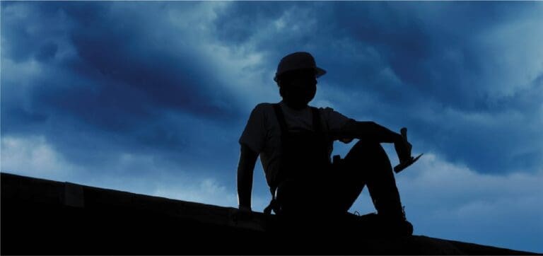 Silhouette of roofer sitting on a roof, resting and appreciating the beginning of the night sky